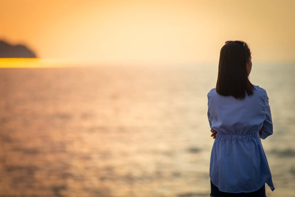 la femme se tient au bord de la mer, le dos tourné et regarde