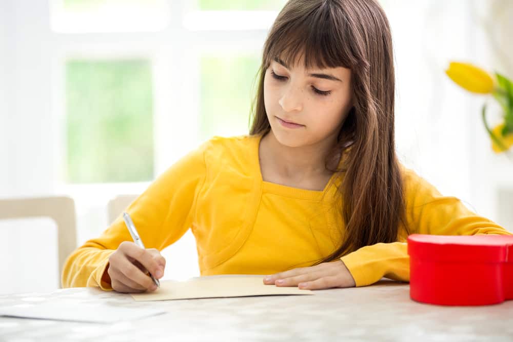 la fille à la table s'assied et écrit une carte de voeux
