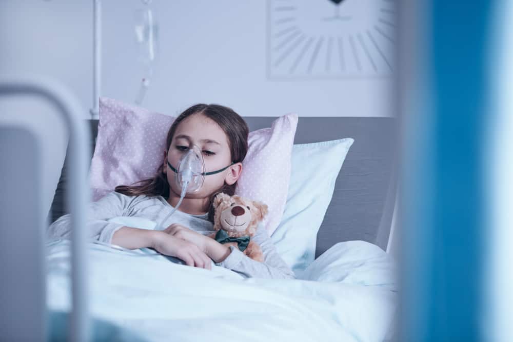 la jeune fille est allongée dans un lit d'hôpital avec un masque à oxygène