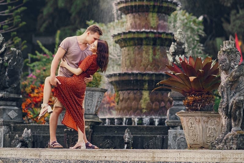 sur la place devant la fontaine se tiennent un homme et une femme dans une étreinte amoureuse