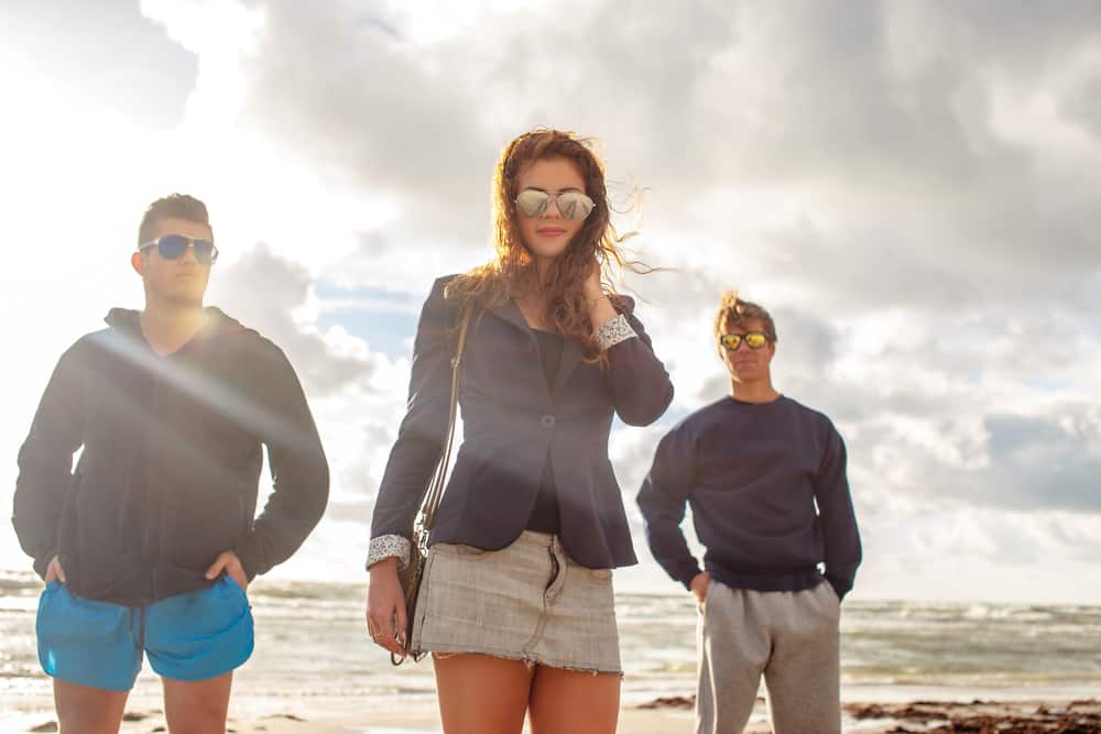 sur la plage se tiennent deux hommes et une femme avec des lunettes de soleil