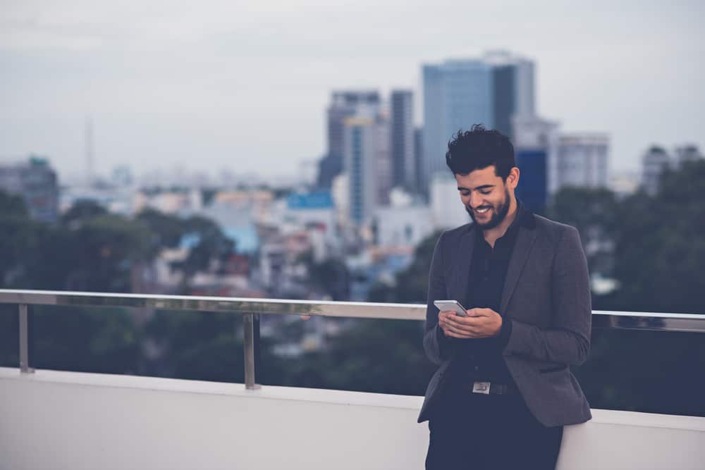un bel homme est debout sur la terrasse et envoie des SMS avec un sourire
