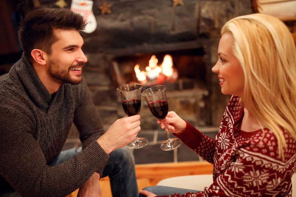 un couple amoureux assis devant une cheminée et griller du vin