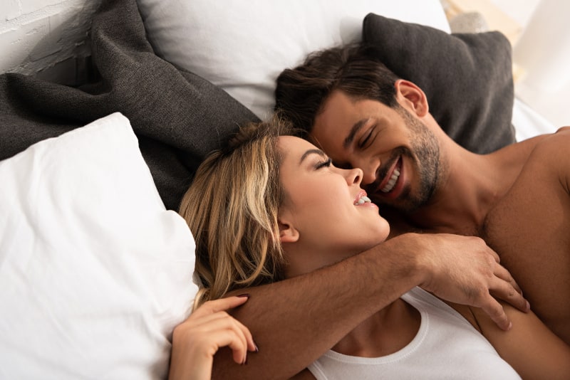 un couple souriant étreindre dans son lit le matin