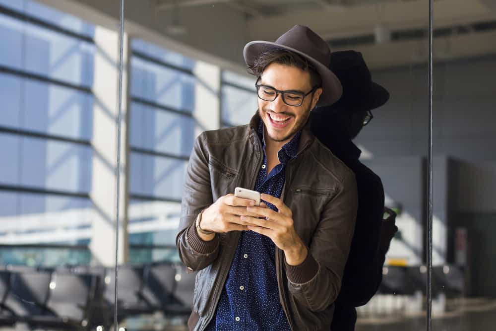un homme avec un chapeau et des lunettes sur la tête écrit des sms