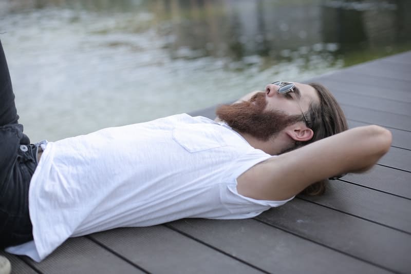 un homme avec une barbe et des lunettes de soleil est allongé sur la jetée