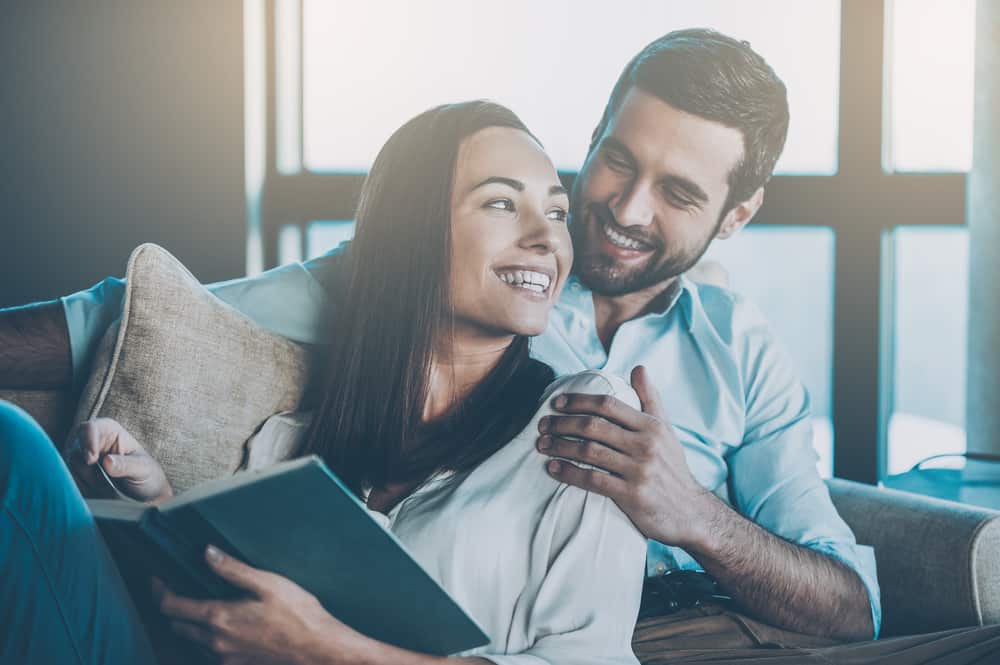 un homme avec une femme rit pendant qu'elle lit un livre et s'assoit dans ses bras
