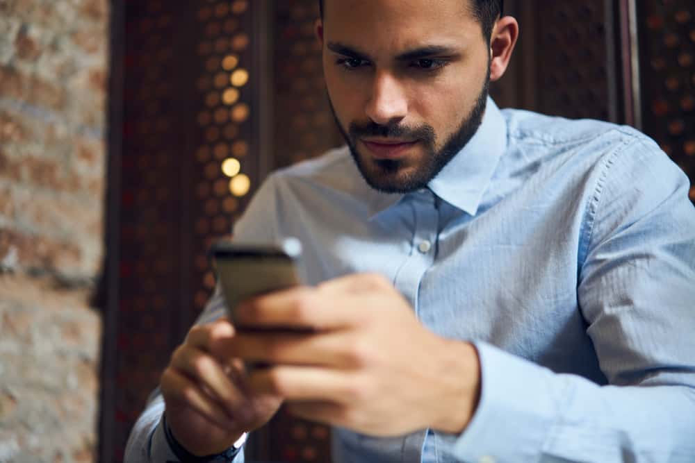 un homme concentré avec une barbe utilise un smartphone