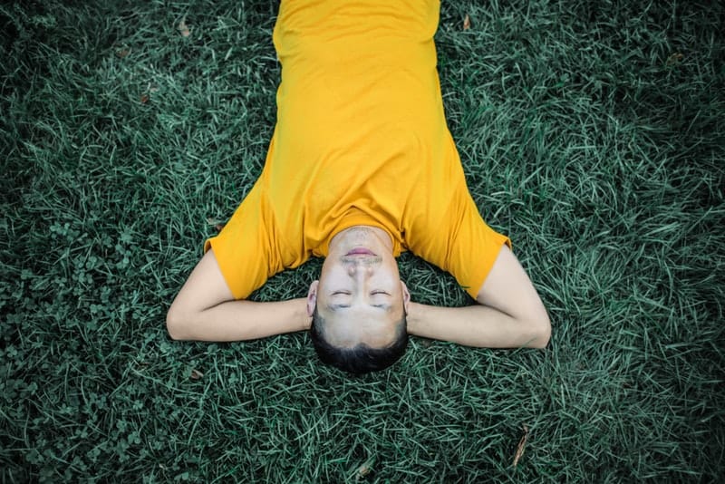un homme dans un t-shirt jaune couché sur l'herbe