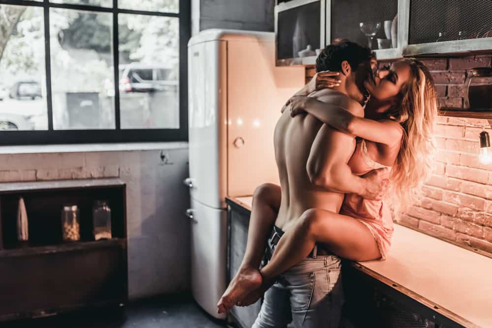 un homme embrasse une femme sur le cou dans la cuisine