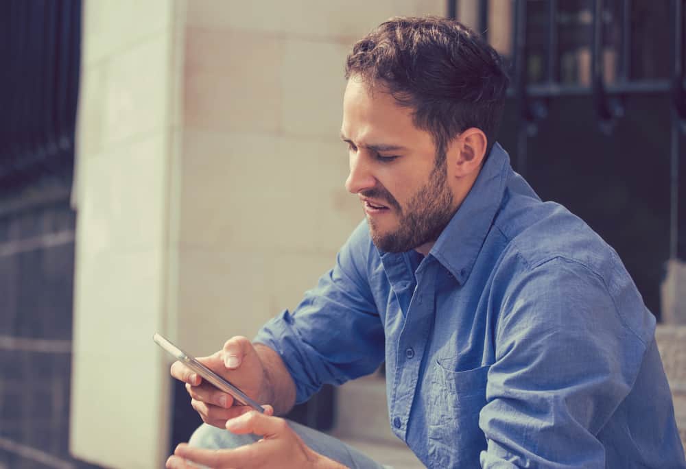 un homme en colère dans une chemise bleue utilise un smartphone