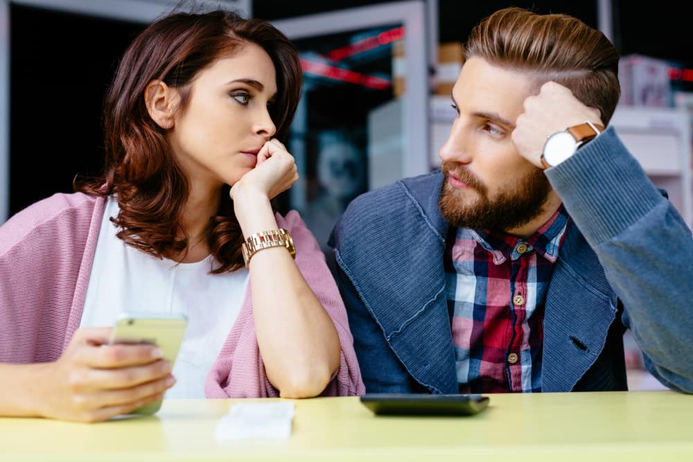 un homme et une femme assis à une table à se regarder pendant qu'elle tient le téléphone dans sa main