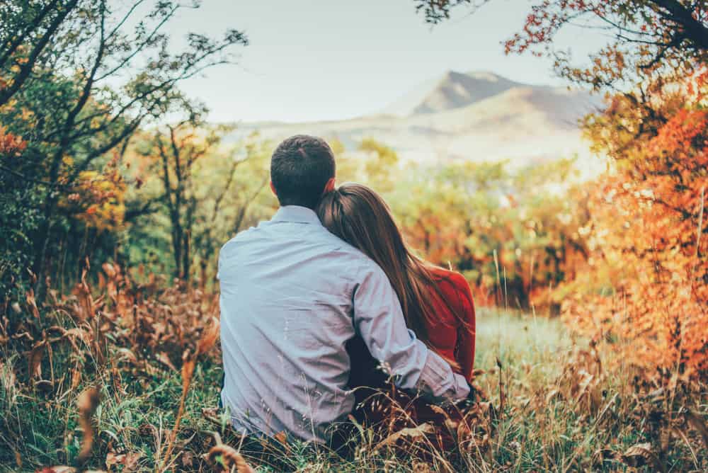 un homme et une femme assis dans la nature embrassant