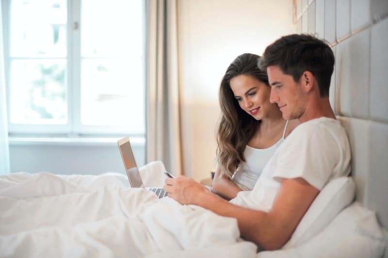 un homme et une femme au lit en regardant un ordinateur portable
