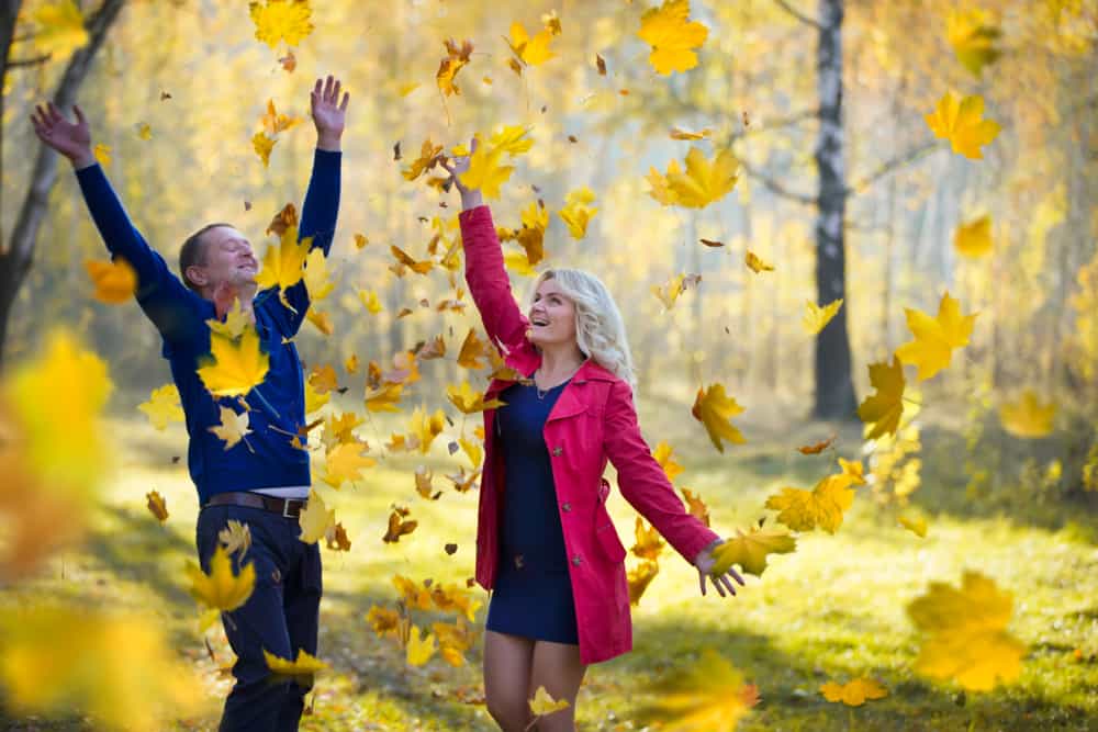 un homme et une femme jettent des feuilles et rient