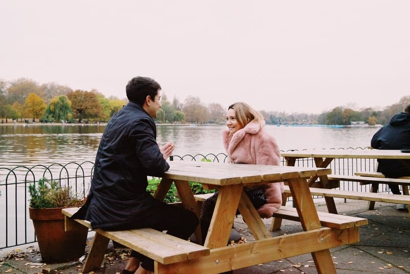 un homme et une femme sont assis sur la terrasse d'un café au bord de la mer et parlent