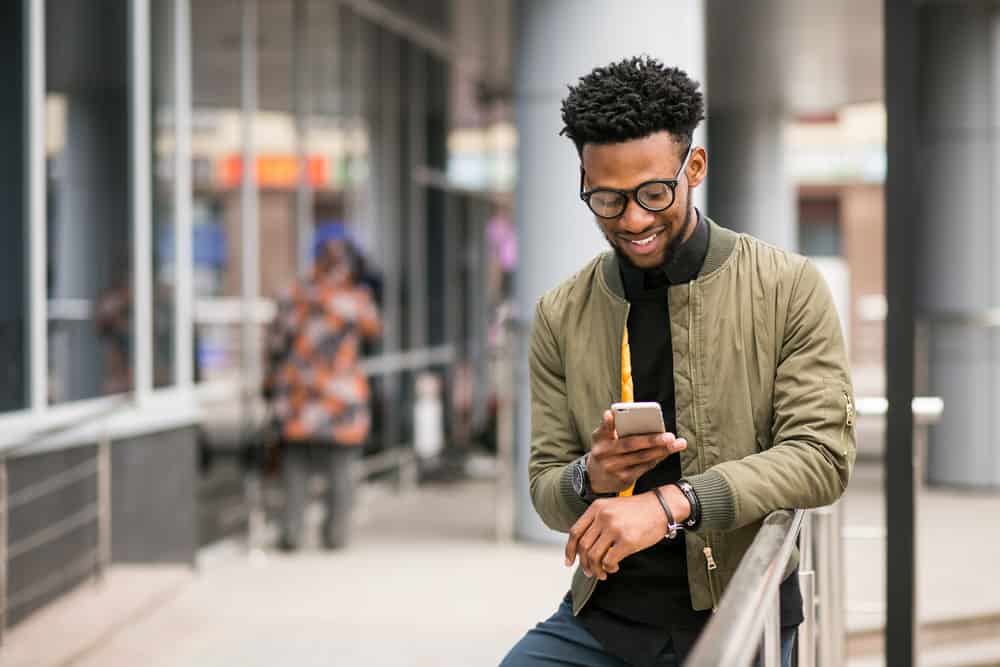 un homme noir se tient près de la clôture et envoie des SMS