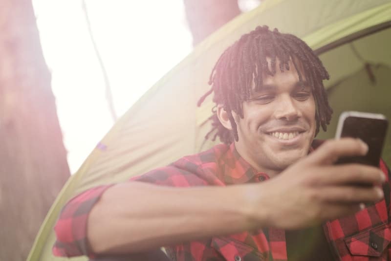 un homme souriant à côté de la tente écrit un sms
