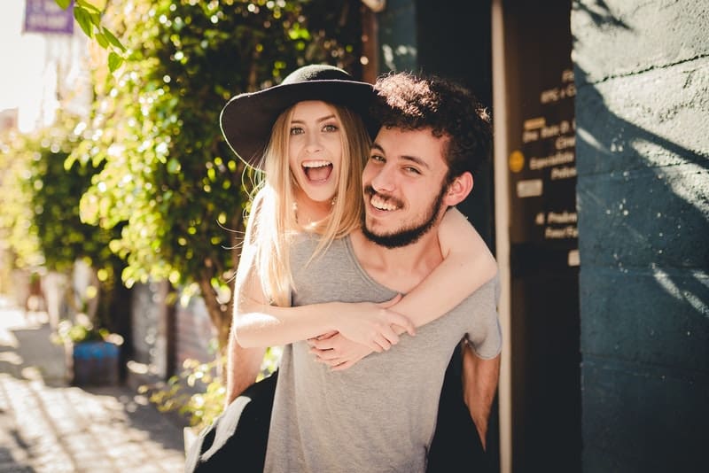 un homme souriant avec une barbe porte sa petite amie sur son dos