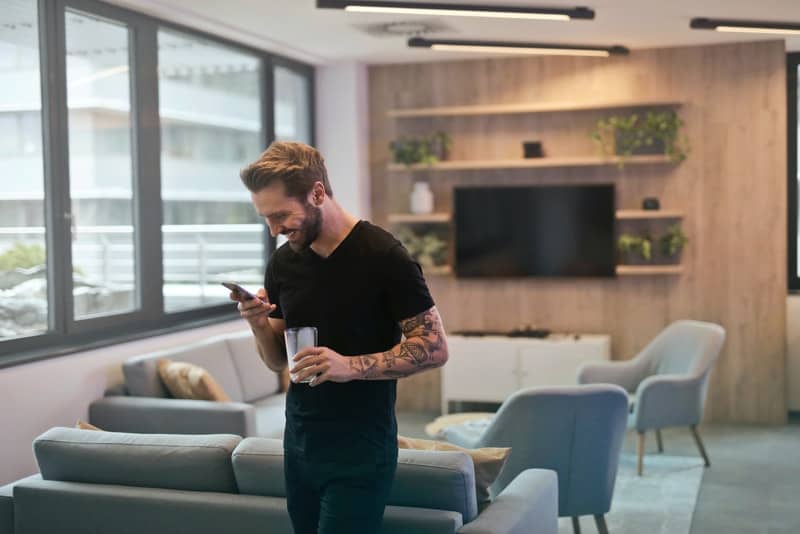 un homme souriant dans l'appartement écrit un sms
