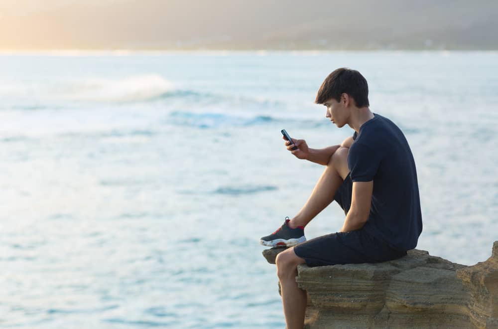 un homme sur un rocher au bord de la mer est assis et un bouton sur le téléphone