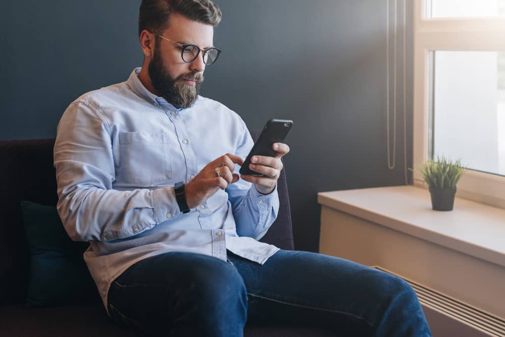 un homme sérieux est assis dans un fauteuil et envoie des SMS