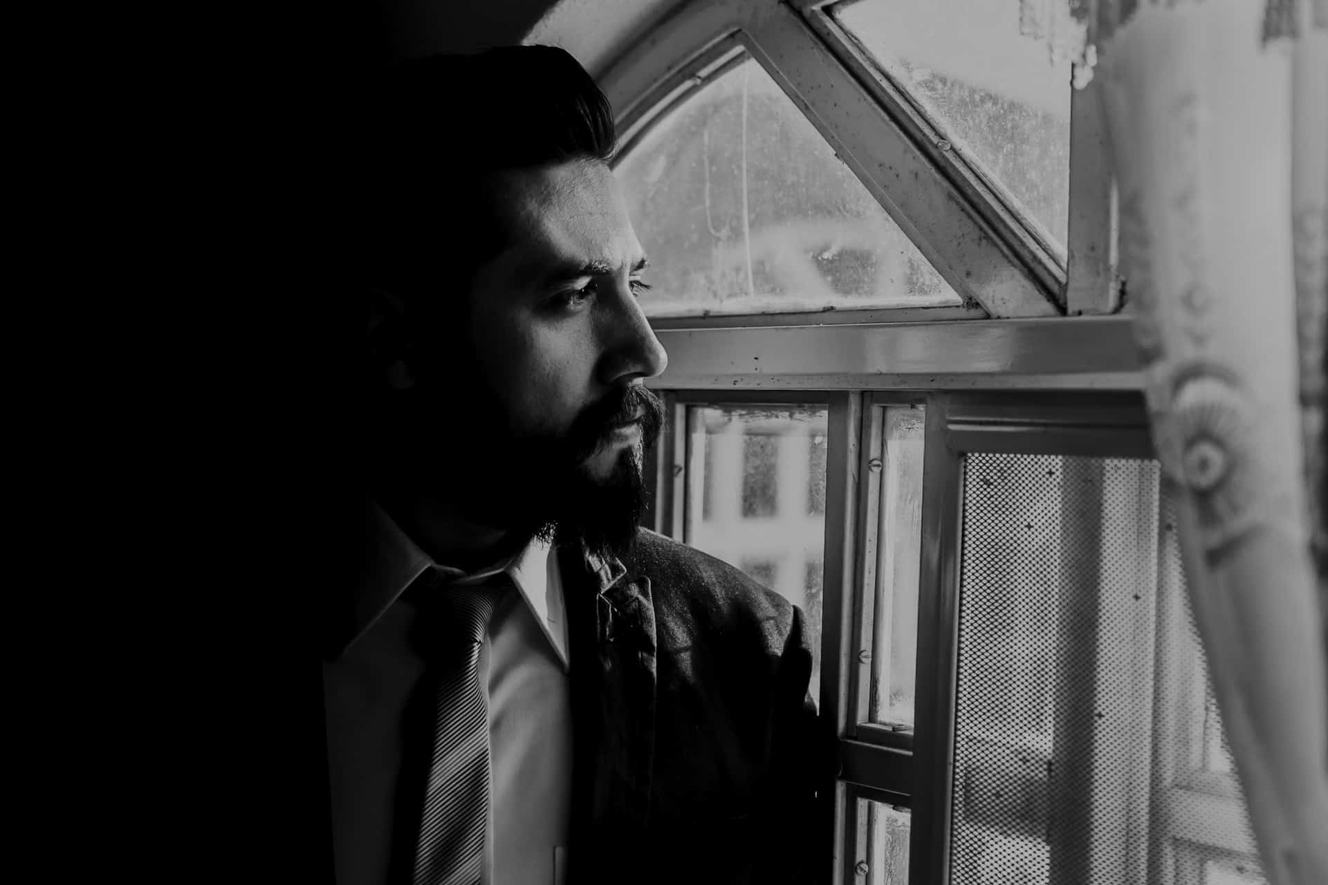 un homme triste avec une barbe regarde par la fenêtre
