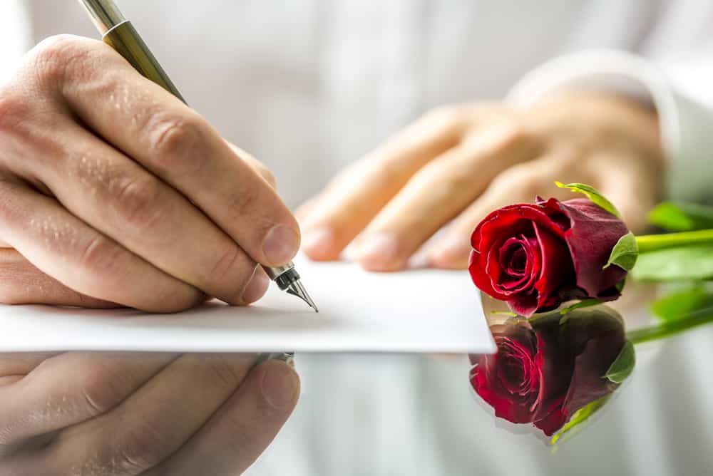 un homme écrit une lettre d'amour à côté de laquelle se trouve une rose rouge