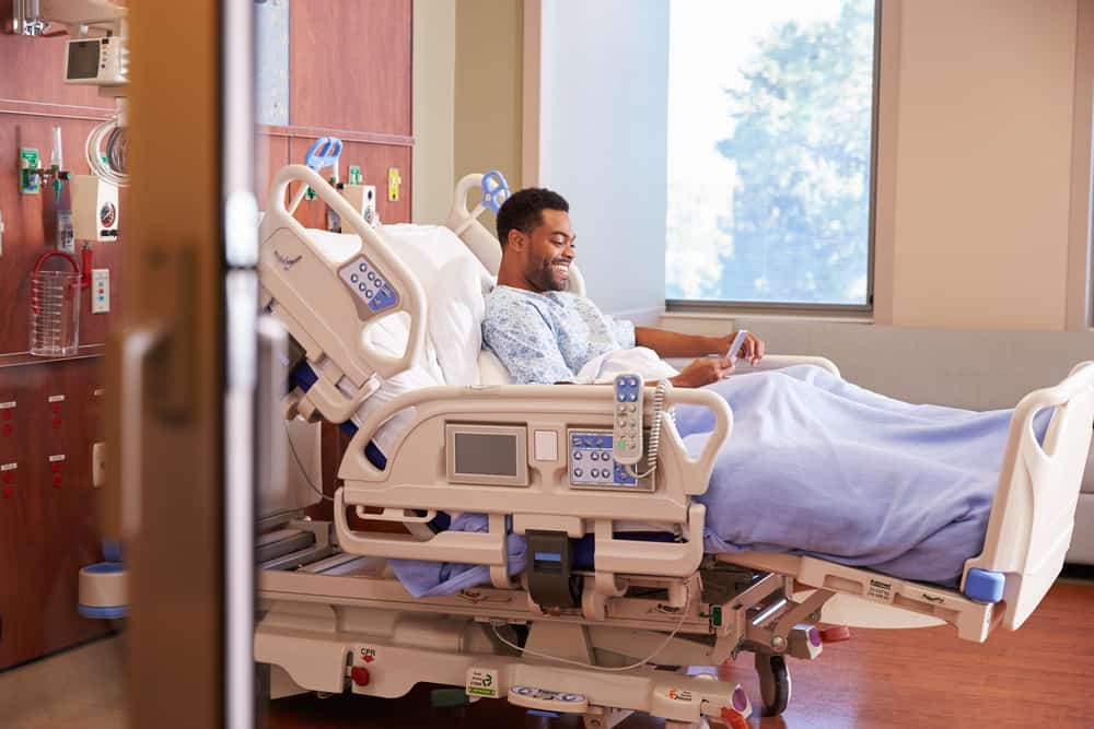 un patient souriant se trouve à l'hôpital et lit un message sur son smartphone
