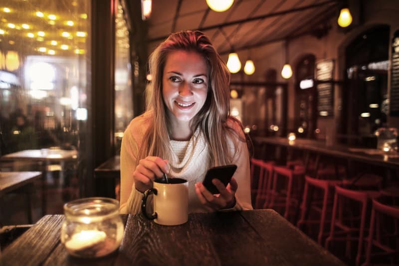 une belle blonde souriante est assise dans un café et tient un téléphone portable dans sa main