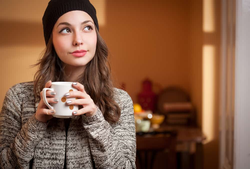 une belle brune avec une tasse de thé dans ses mains se tient dans la chambre