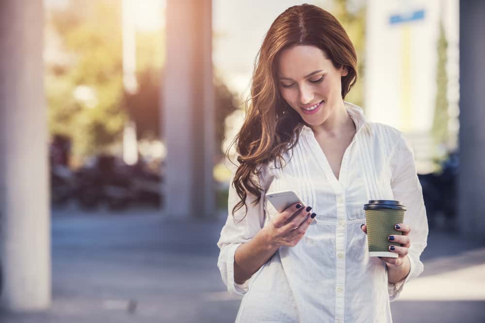 une belle femme dans une chemise blanche se tient à l'extérieur et utilise le téléphone