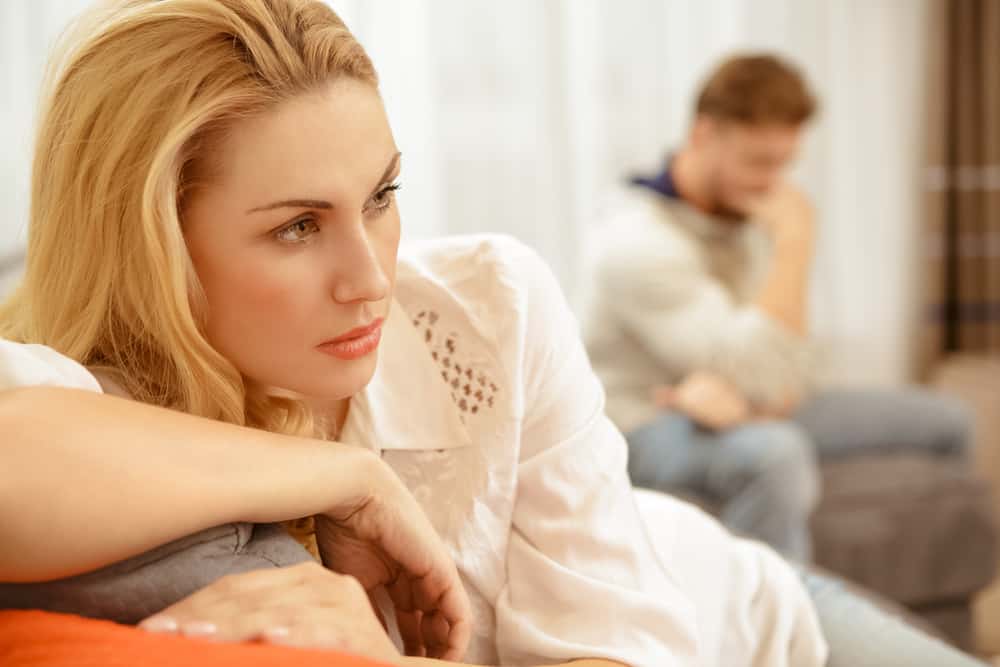 une blonde pensive est assise sur le canapé avec son homme