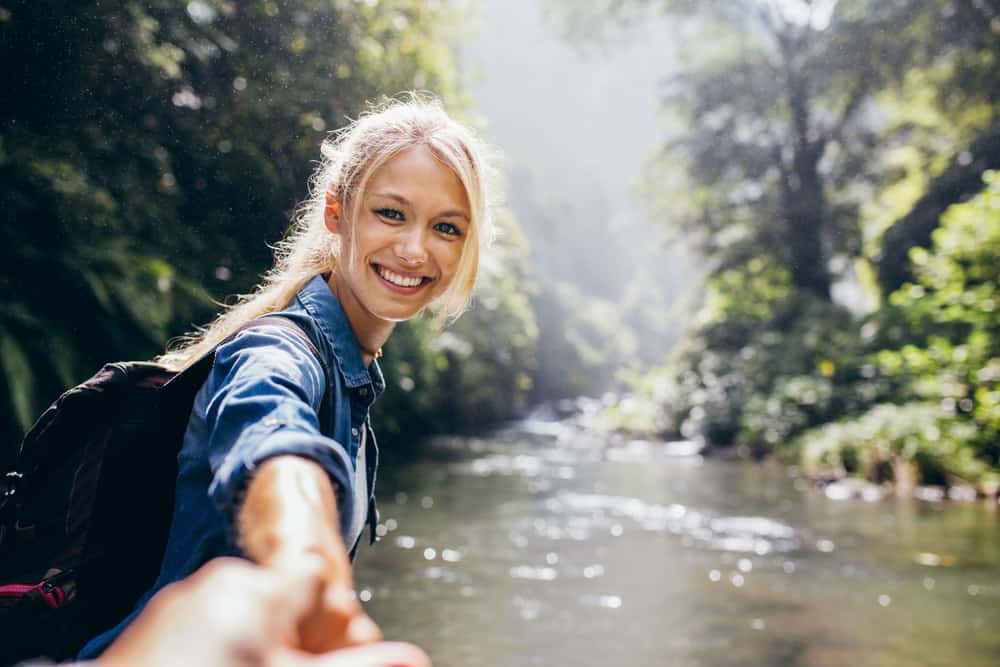 une blonde souriante au bord de la rivière tient la main d'un homme