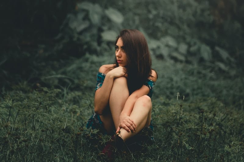 une brune dans une robe d'été est assise sur l'herbe