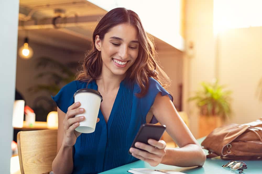 une femme assise avec du café à la main et un téléphone