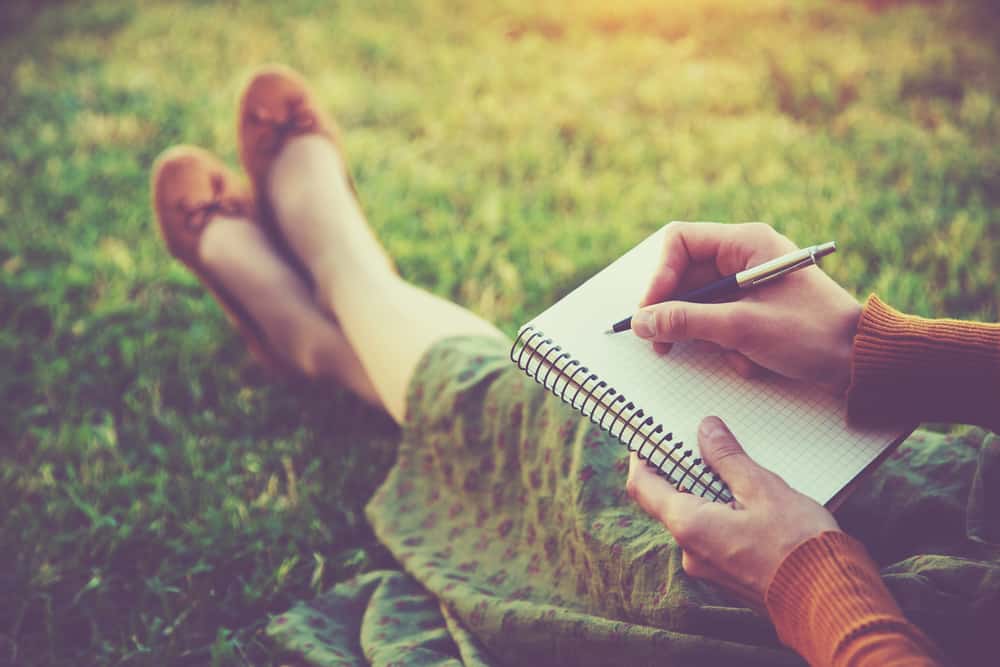une femme assise dans l'herbe et écrit