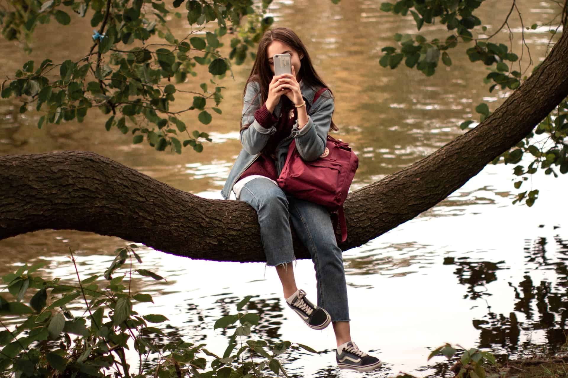 une femme assise dans un arbre avec un téléphone à la main