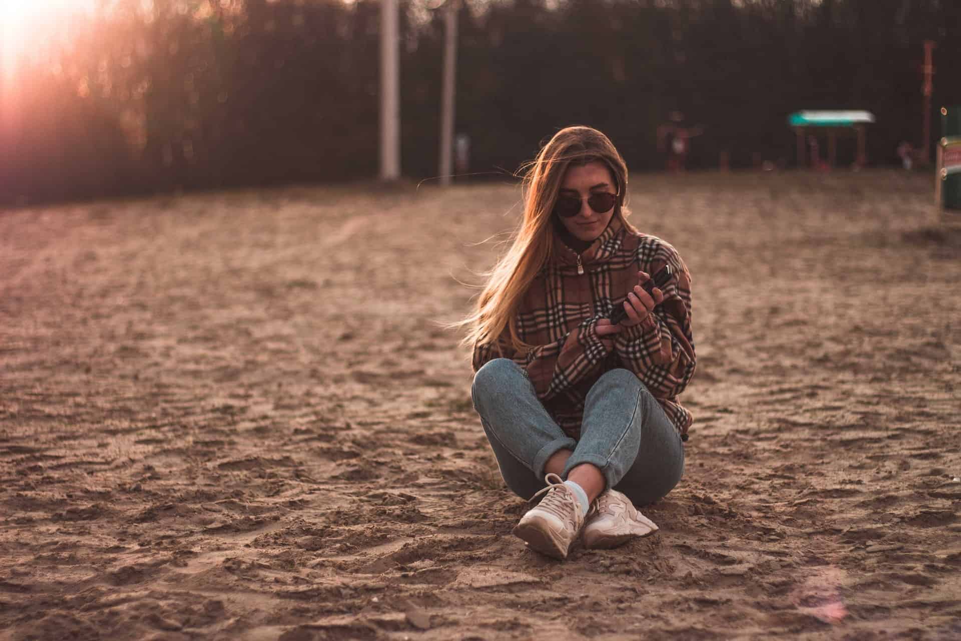 une femme assise sur l'herbe avec un téléphone à la main