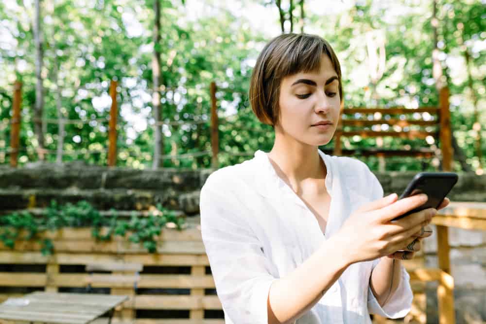 une femme aux cheveux courts se tient dehors et utilise un téléphone portable