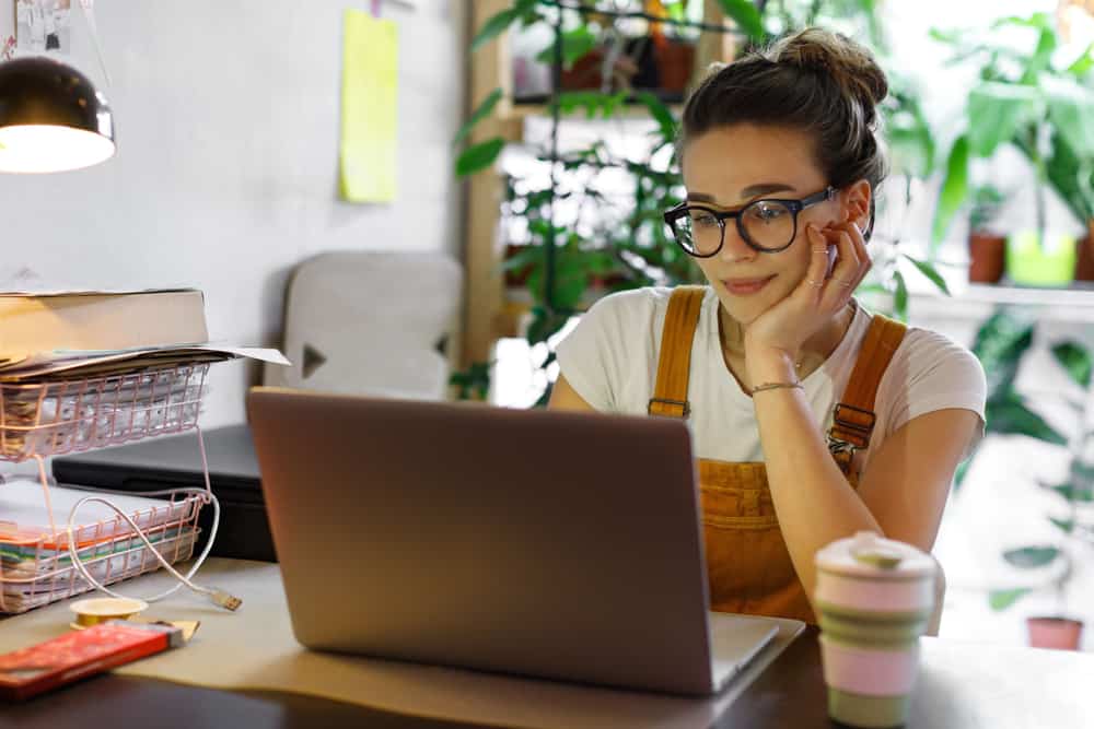 une femme avec des lunettes est assise et travaille derrière un ordinateur portable