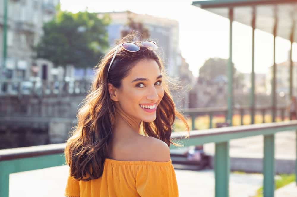 une femme avec des lunettes sur la tête et une chemise jaune rit
