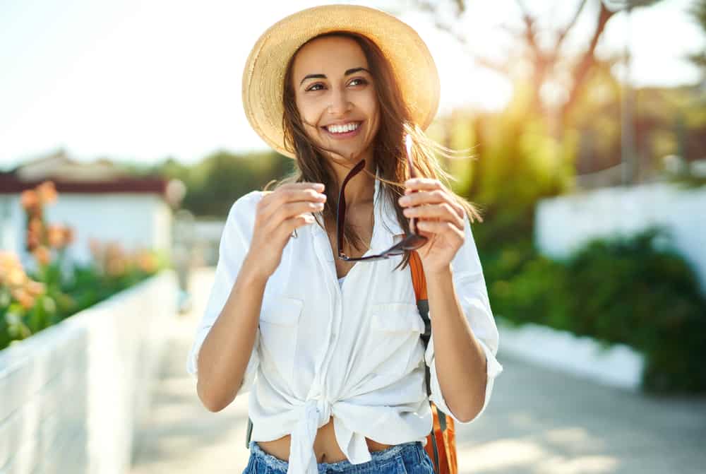 une femme avec un chapeau sur la tête et des lunettes à la main rit