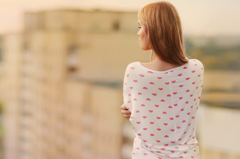 une femme bleue se tient sur un balcon, le dos tourné