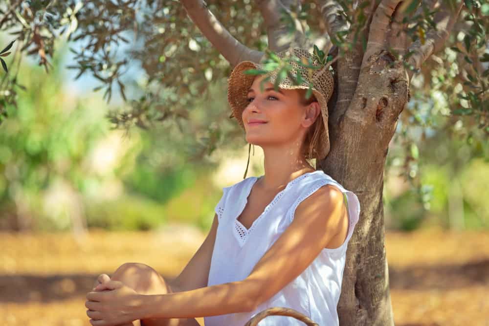 une femme blonde est assise près d'un arbre et sourit