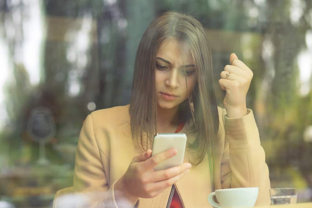 une femme en colère est assise dans un café et à l'aide d'un smartphone