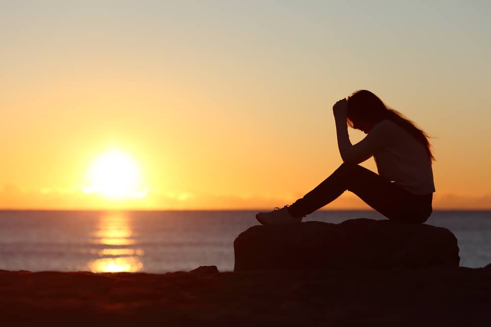 une femme est assise à côté d'une jetée au coucher du soleil