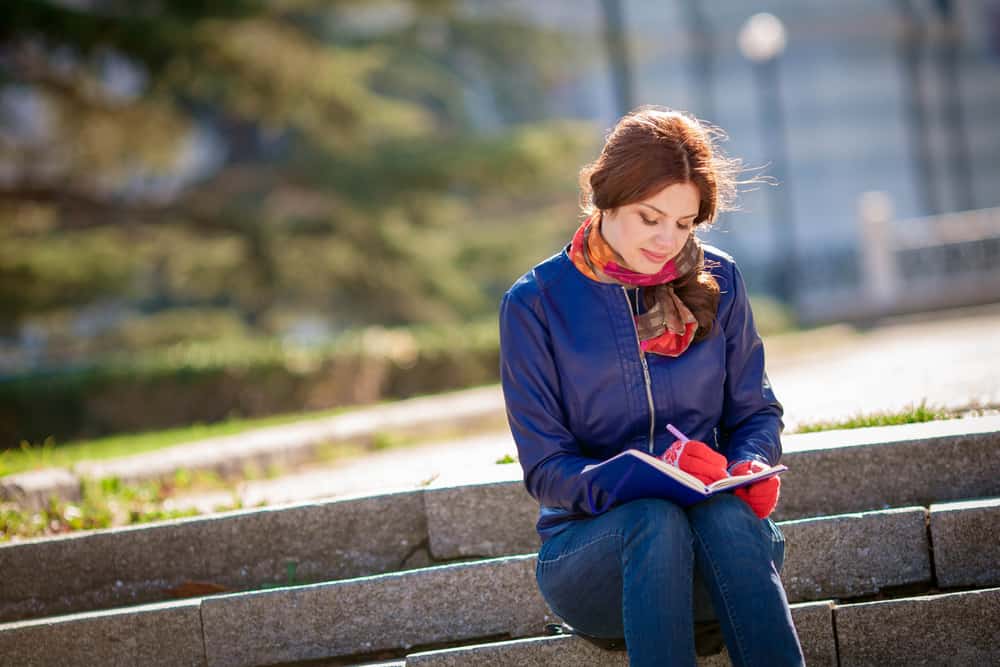 une femme est assise dans les escaliers et écrit dans son journal