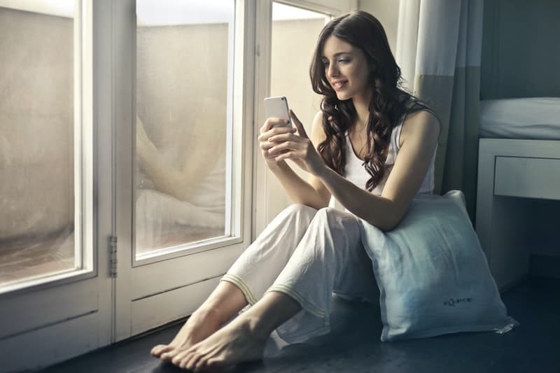 une femme est assise près de la fenêtre et écrit au téléphone