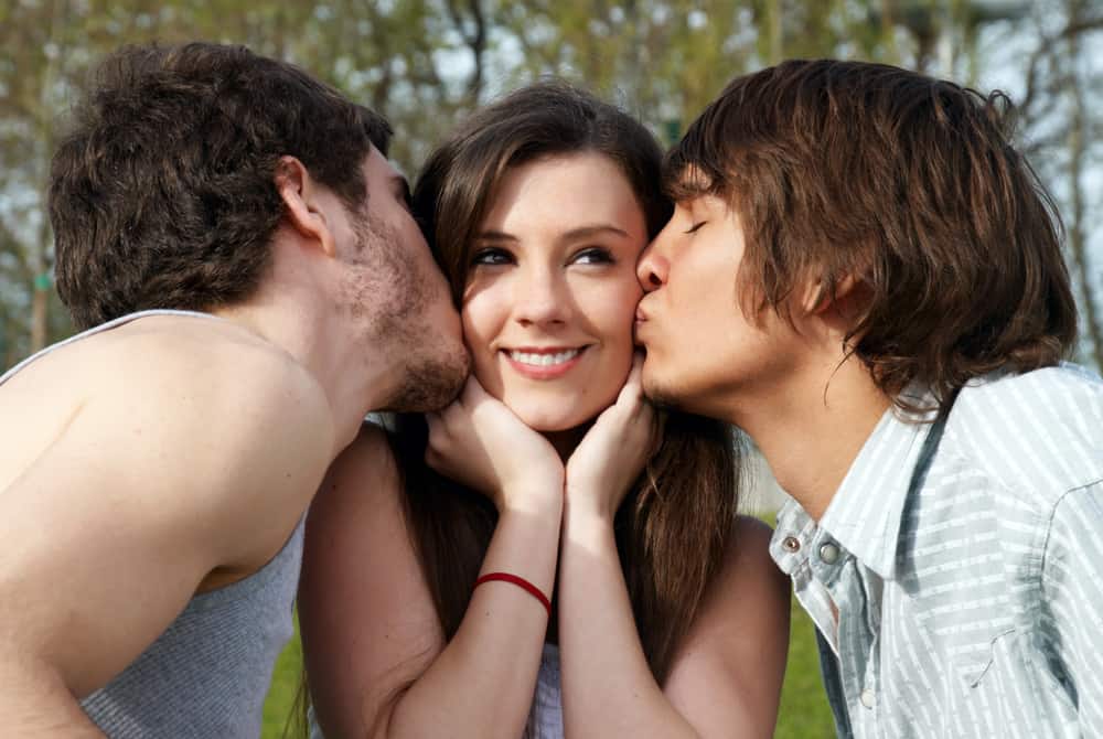 une femme heureuse sur le côté est embrassée par deux hommes sur les joues